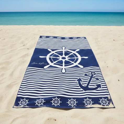 Toalla de playa marinera de 90x170 cm en color azul marino y blanco con diseño de timón, ancla y rayas, extendida sobre la arena